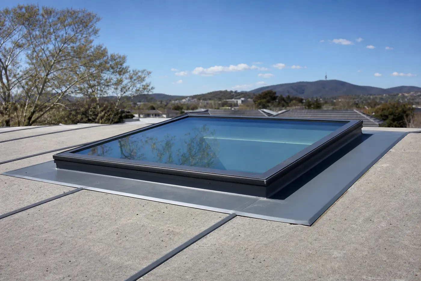 A flat glass skylight installed into a concrete-tile Canberra roof with fresh metal flashing around its edges
